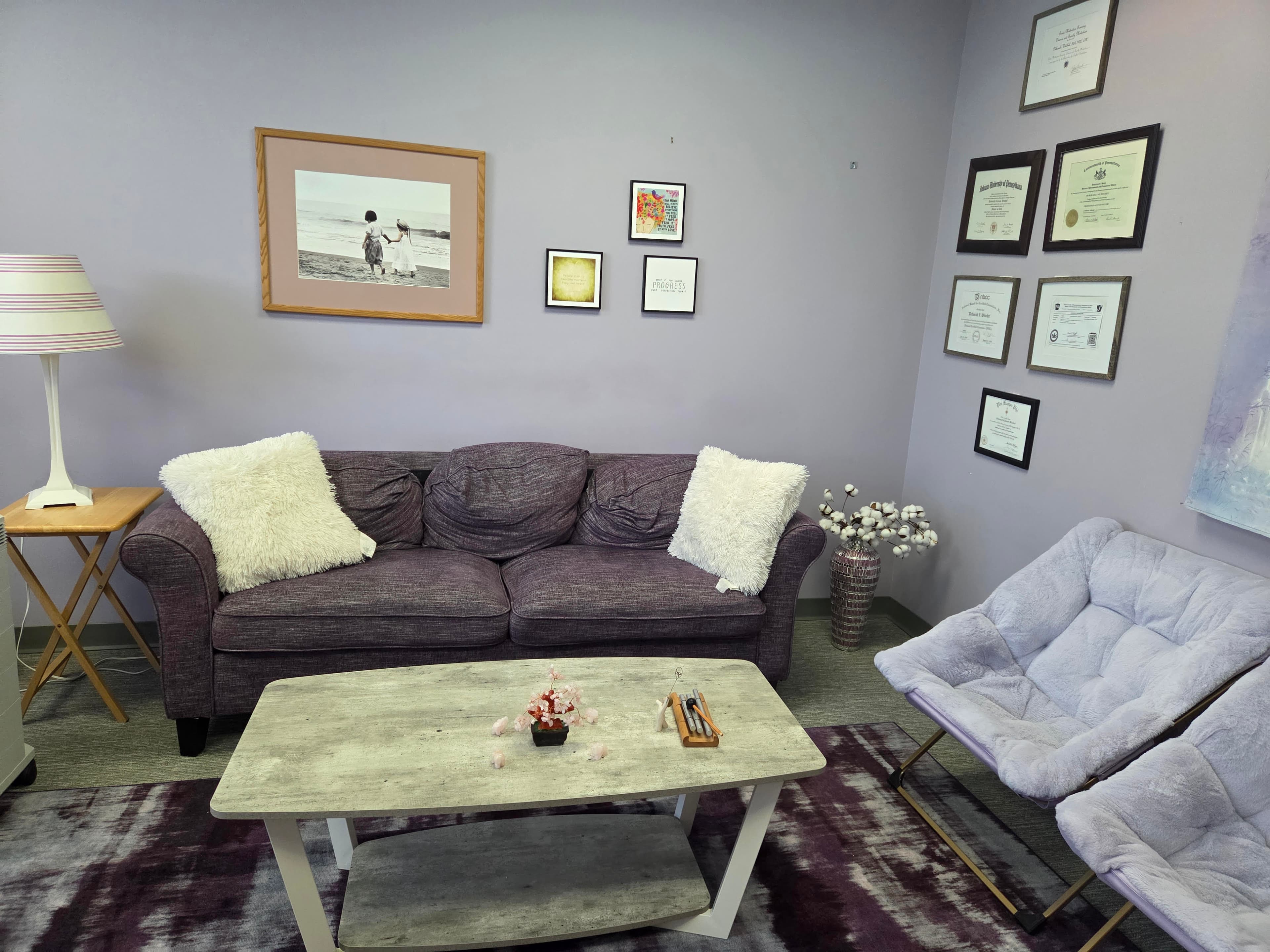 Therapy office interior showing comfortable seating area with purple sofa, chairs, and professional decor